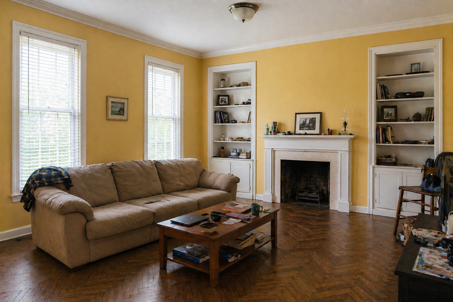 Dated mustard yellow living room before makeover with worn tan sofa and venetian blinds
